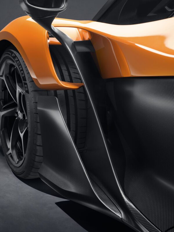 Close-up of an orange McLaren W1 sports car featuring carbon fiber detailing and black wheels.