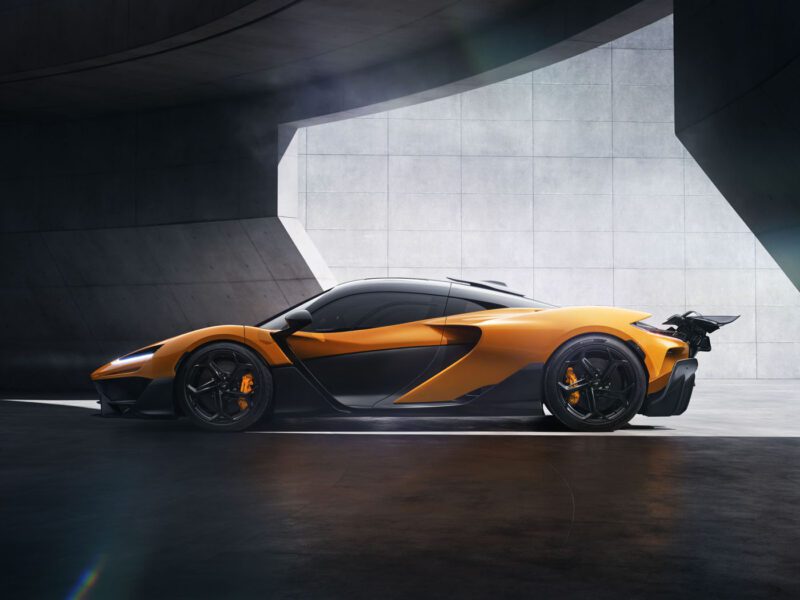 A sleek orange McLaren sports car with black accents is parked in a modern concrete structure, exuding an aura of luxury and precision.