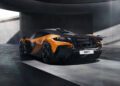 The McLaren W1, with its orange and black finish, is showcased from the rear in a concrete garage. Sunlight streams through the openings above, highlighting its sleek design and advanced 3D printed suspension.