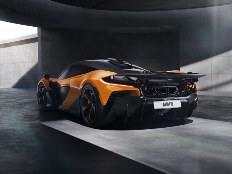 A sleek orange McLaren sports car, boasting impressive specs, is parked in a modern concrete structure. Its rear view highlights aerodynamic features and a visible license plate.