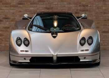 Front view of a sleek, silver Utopia Roadster with four headlights, parked indoors in front of a brick wall, echoing the elegance found at Pagani Displays.