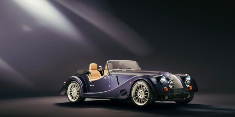 A classic-style black convertible, the 1-of-30 Plus Six Pinnacle by Morgan Sends Off, features a tan interior and is elegantly showcased under dramatic lighting against a dark background.