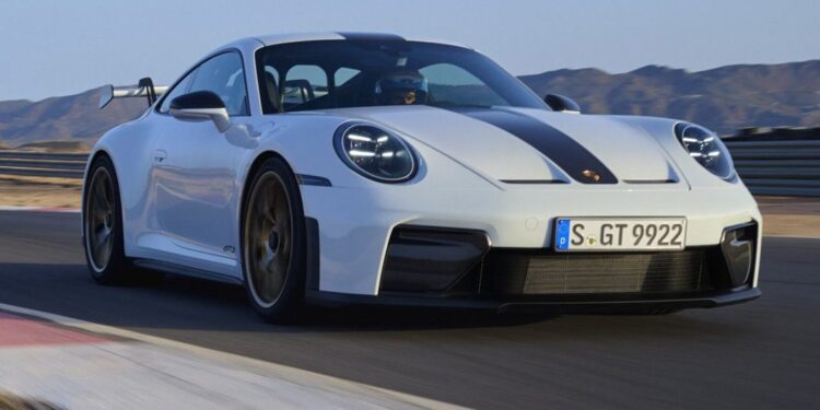 A white Porsche 911 GT3 with a black stripe speeds down the racetrack, mountains towering majestically in the background.