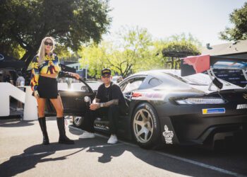 A woman and a man are posing beside a sleek Mercedes-Benz sports car, set against the vibrant backdrop of trees and event tents at the United States Grand Prix in Austin.