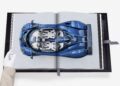 A gloved hand holds open an Assouline book, displaying an image of a blue sports car from a top-down view, showcasing one of its rare cars.