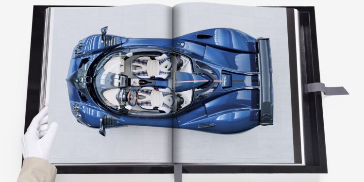 A gloved hand holds open an Assouline book, displaying an image of a blue sports car from a top-down view, showcasing one of its rare cars.