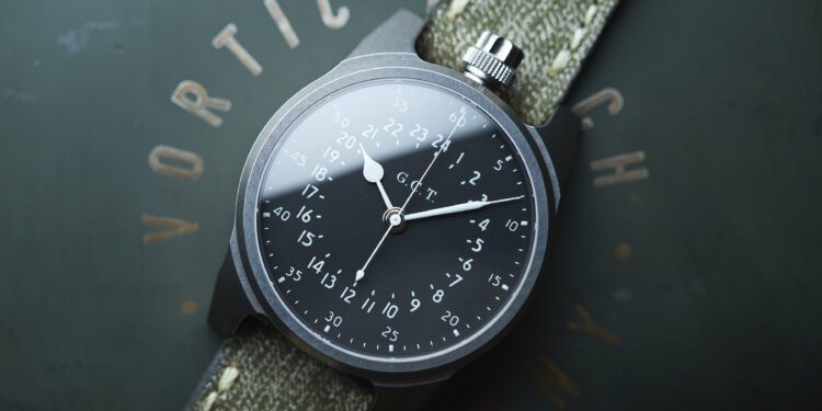 A vintage wristwatch with a dark dial displaying military time numerals and white hands on a green fabric strap lies on a flat surface, showcasing American craftsmanship reminiscent of the Vortic Watch Company's timeless elegance.