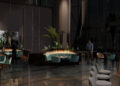 The modern restaurant interior exudes luxury with its dim lighting, green plants, and round tables surrounded by chairs. In this elegant setting akin to Bentley Residences, two people are seated while another walks past large windows in the background.