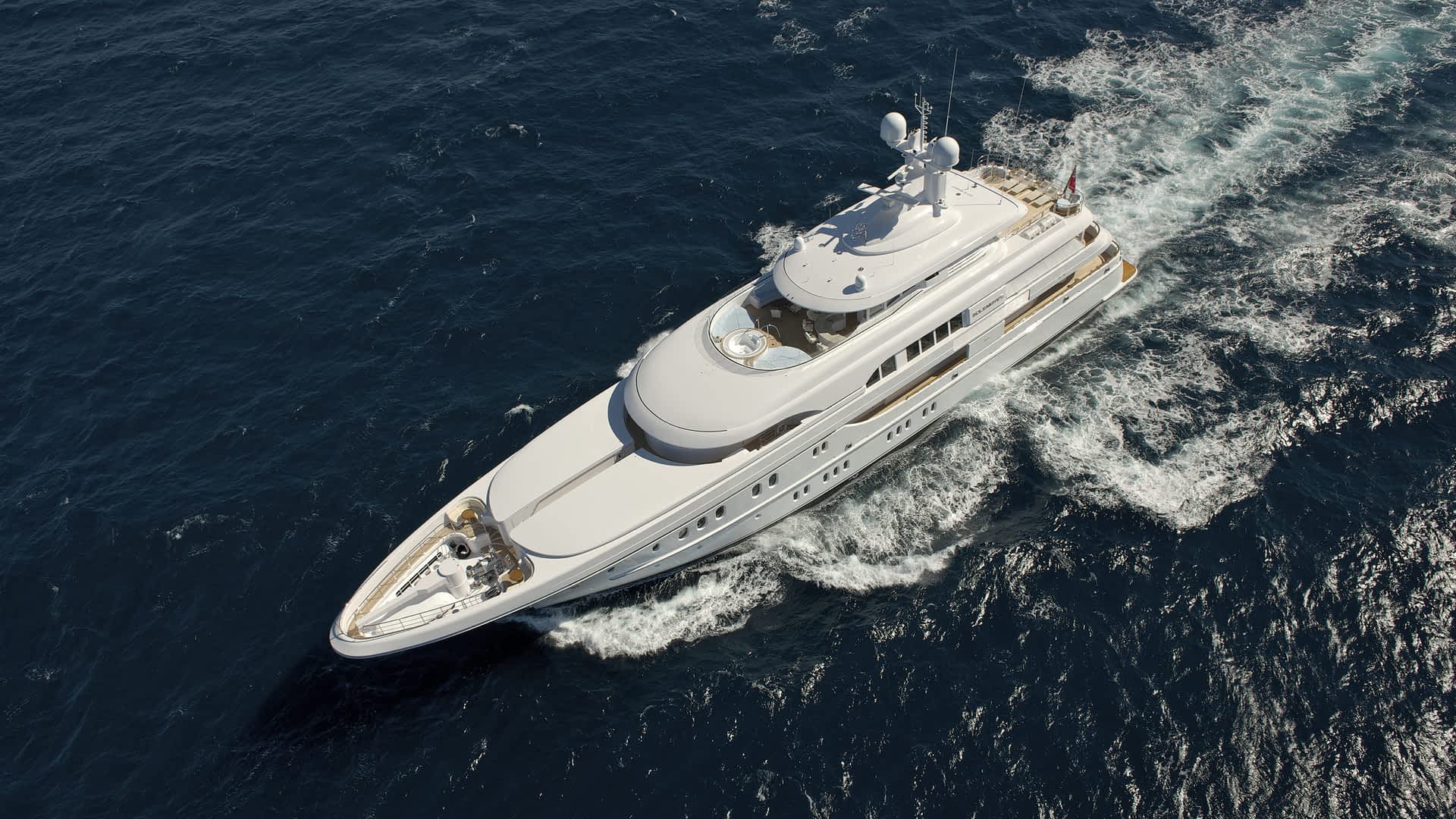 A luxury yacht cuts through the open sea, its sleek white form viewed from above as it creates a mesmerizing wake. Could this stunning vessel be a glimpse of what awaits at the 2024 Fort Lauderdale International Boat Show?