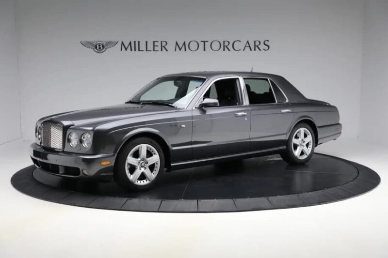 A gray sedan, one of the best bentleys, is displayed on a rotating platform in a showroom with "Miller Motorcars" Signs in the background.