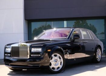 A black Rolls-Royce Phantom luxury sedan is parked in front of a modern building with large windows and a white-and-gray facade.