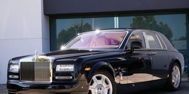 A black Rolls-Royce Phantom luxury sedan is parked in front of a modern building with large windows and a white-and-gray facade.