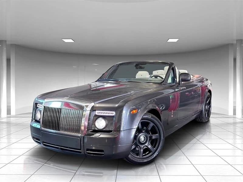A black Rolls-Royce Phantom convertible with the top down, this luxury sedan is parked indoors on a white tiled floor under bright ceiling lights.