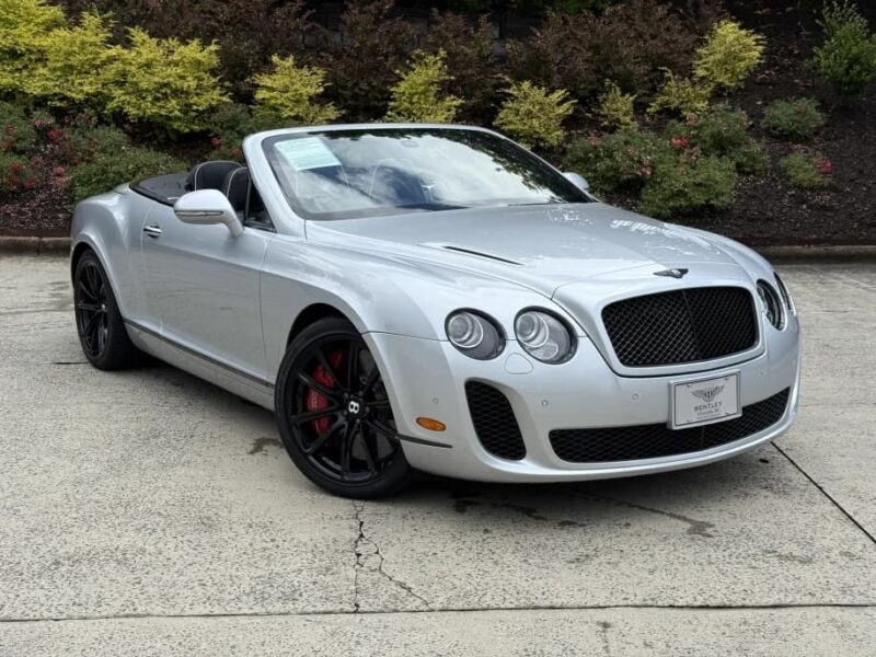 Silver Bentley convertible with black wheels, stopped on a concrete corridor surrounded by green spaces - an amazing example of the best inspiration and ideal inspiration for anyone browsing Bentleys for sale.