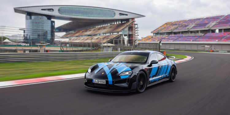 A sleek, black and blue Turbo GT sports car speeds around the racetrack at Shanghai International Circuit, with grandstands and a modern building in the background.