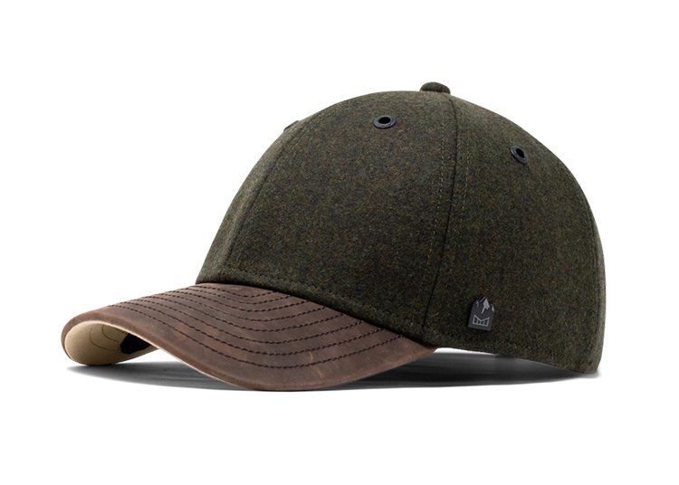 A green wool cap with a brown leather brim and black eyelets is tilted on a white surface, perfect for the cooler months outlined in the Fall Shopping Guide.