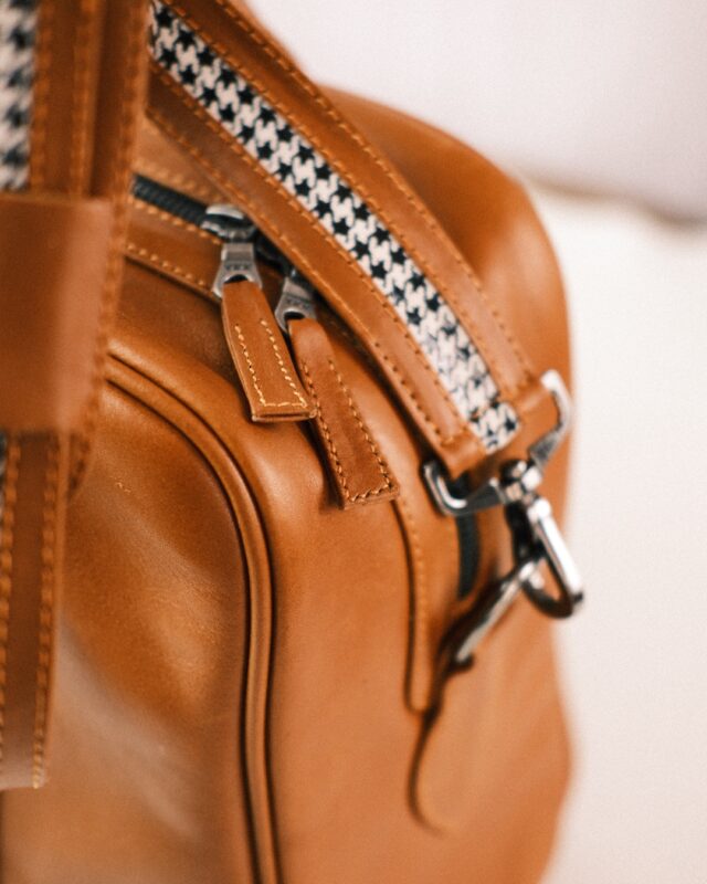 Close-up of a brown leather bag with custom luggage-inspired patterned straps and silver hardware.