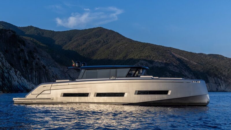 A sleek, modern luxury yacht glides on calm water with rugged mountains under a clear sky, reminiscent of the stunning displays at the 2024 Fort Lauderdale International Boat Show.