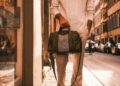 A person strolls down the street carrying a green and white bag, their ensemble completed with a light sweater and bespoke jacket.