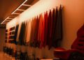 A row of colorful fabric samples hangs on a wall, with car wheels displayed below, in a well-lit showroom showcasing Walter Leather Bespoke creations. A red car seat is visible on the right, hinting at the luxury of custom leather jackets and luggage.