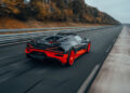 A sleek black and red Bugatti W16 Mistral races down an empty highway, trees blurring in the background, as if chasing a world record.