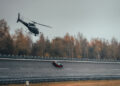 A helicopter flies above a Bugatti W16 Mistral on a sloped road, with autumn trees painting the background. This marvel, boasting a 282 MPH top speed, commands admiration and whispers of world records in its wake.