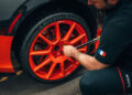 A person tightens the lug nuts on an orange car wheel, prepping for a performance that could rival the Bugatti W16 Mistral's world record top speed.