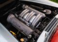 Close-up of a vintage 1957 Mercedes-Benz car engine with silver and metallic components, intricate piping, and a dark surrounding area under the open hood.