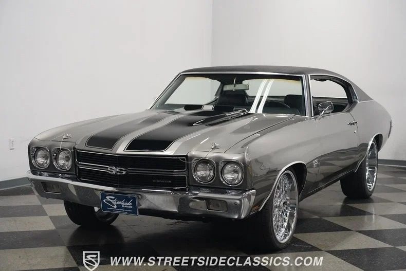 A high-performance silver classic muscle car with black racing stripes shines in a showroom setting.