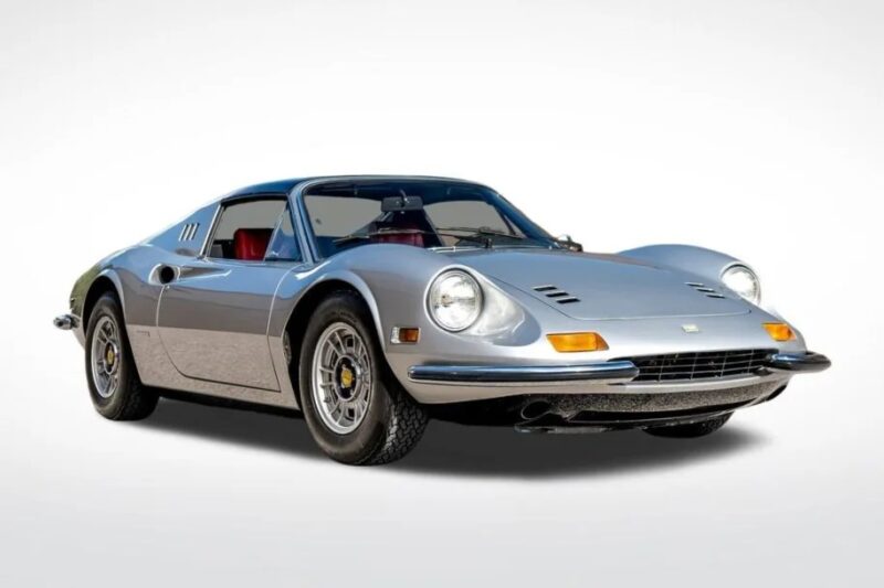 Vintage silver Ferrari Dino sports car with a sleek design, prominent headlights, and classic mid-engine layout on display. White background enhances these exquisite cars for sale.