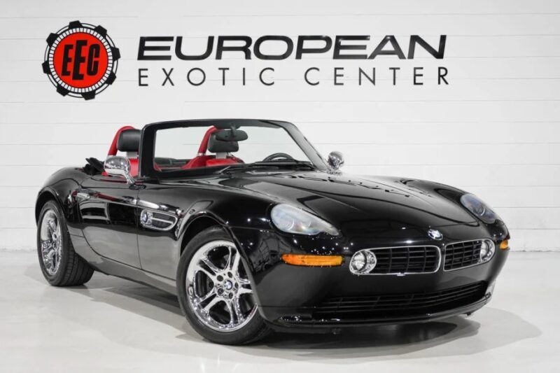 A black convertible sports car, a modern classic BMW Z8, is parked indoors with a European Exotic Center sign in the background.