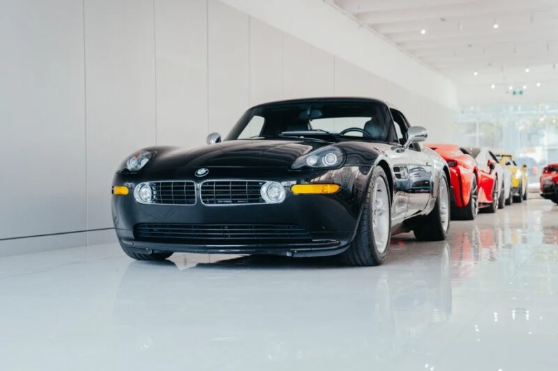 A modern classic, the sleek black BMW Z8 sports car is parked indoors, lined up elegantly with other cars in a well-lit showroom.