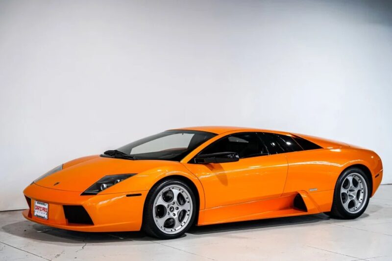 Orange sports car with sleek 2000s design, parked indoors on a white floor, angled to the left.