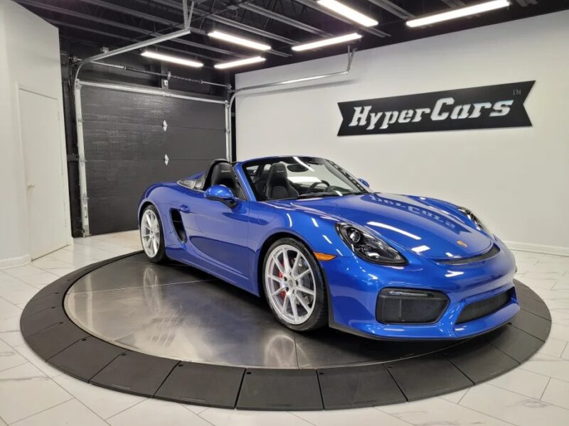 A blue convertible sports car with a manual transmission dazzles in a modern showroom on a rotating platform, flaunting white wheels beneath the "HyperCars" sign. Discover the best manual cars and buy today to experience the thrill firsthand.