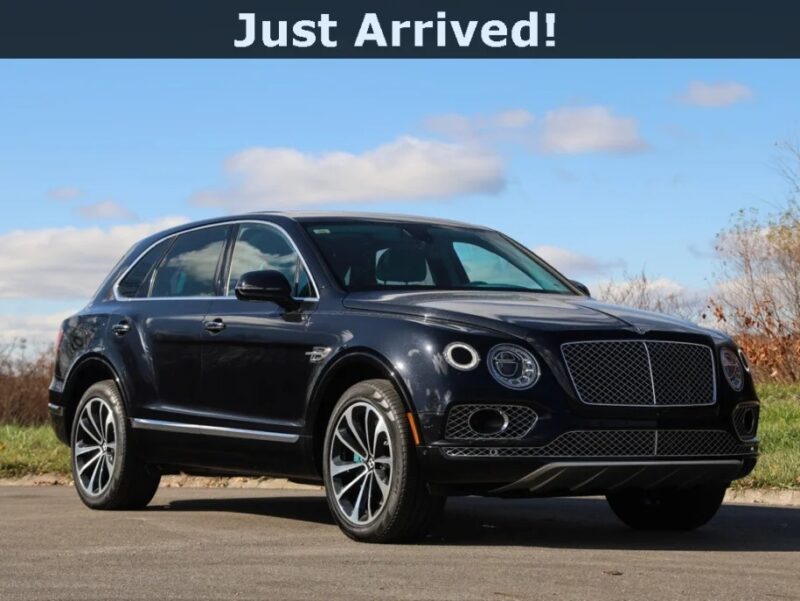 A black Bentley Bentayga, the epitome of an Ultra-Luxe SUV, is parked on a paved surface under a partly cloudy sky. Text above reads, "Just Arrived!".