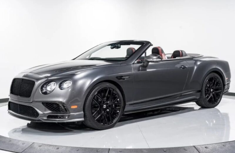 A sleek gray Bentley Continental GTC with black rims and a black grille is parked indoors. This luxury tourer boasts an exquisite red and black interior, perfectly complementing its elegant exterior.