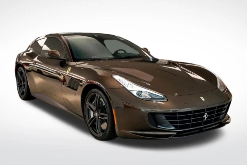 A brown Ferrari sports car with black wheels, showcasing one of the unique Ferrari colors, is parked on a plain white background and viewed from the front left side.
