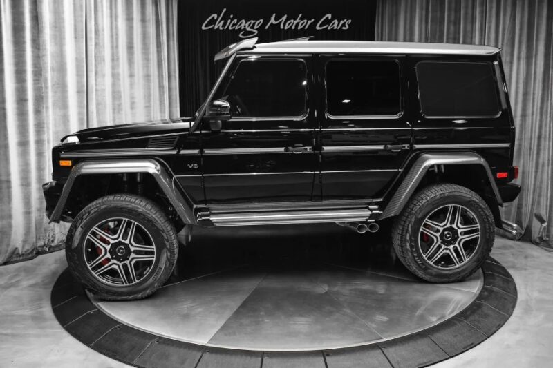 SUV Black Mercedes-Benz G-Class mewah ditampilkan dengan selera tinggi pada platform melingkar, dibingkai oleh tirai elegan di latar belakang.