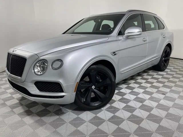 The ultra-luxe silver Bentley Bentayga SUV, featuring sleek black wheels, glimmers on the checkered floor of a well-lit showroom.