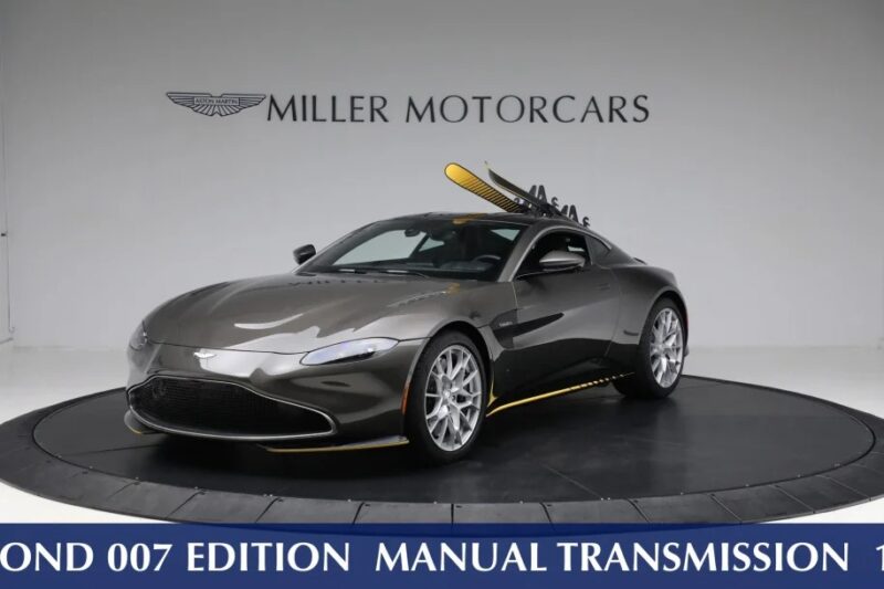 The Aston Martin sports car takes center stage in the showroom beneath a "Miller Motorcars" sign, showcasing the "James Bond 007 Edition." It's a standout among the best manual cars for those looking to buy a manual transmission that's both iconic and sleek.