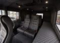 Interior of a luxury vehicle with black leather seats, quilted side panel, and carpeting. The design features two rows of seats, lighting, and a spacious cabin.