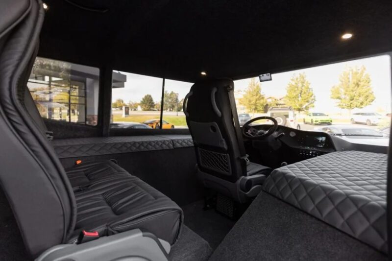 Interior of a luxury vehicle showing a driver's seat, dashboard, and quilted seating area in the back, viewed from the rear passenger side.