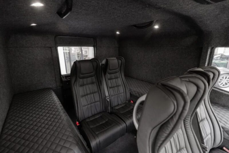 Interior of a vehicle featuring black quilted upholstery, three black seats, and overhead lights.