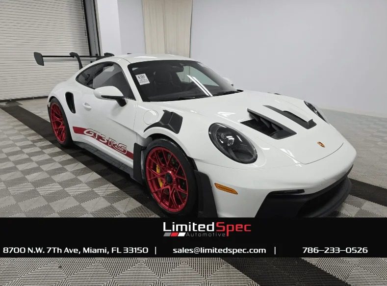 Porsche 911 GT3 RS, the ultimate driver's car, shines indoors with red rims against a checkered floor. Company contact details at the bottom.