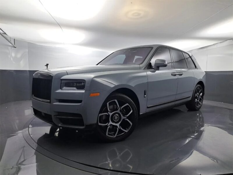 A silver Ultra-Luxe SUV, possibly a Rolls-Royce Cullinan or Bentley Bentayga, is elegantly parked in a well-lit, minimalist indoor space with reflective floors.