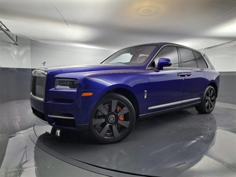 A blue Rolls-Royce Cullinan is parked in a sleek, modern showroom with reflective floors, epitomizing the ultra-luxe SUV experience.