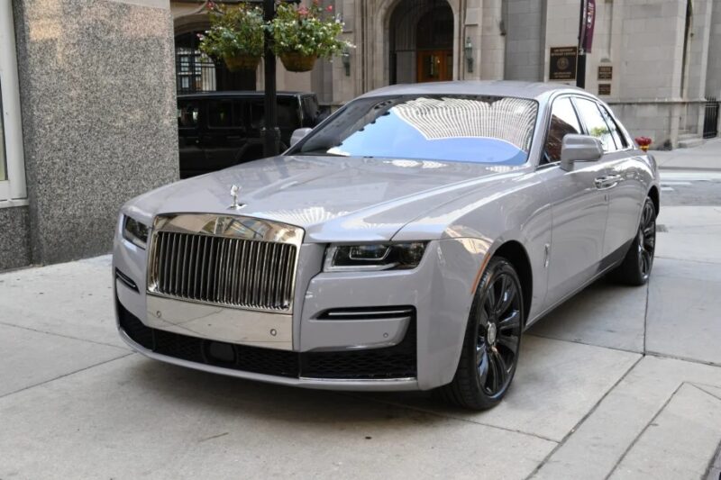 A gray luxury sedan is parked on a city street, featuring a shiny grille and sleek design, boasting one of those powerful V12 engines that makes it an exotic car.