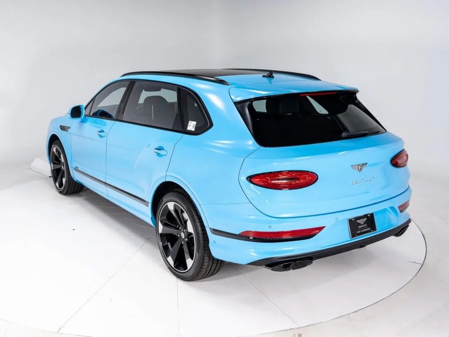 A bright blue Bentley Bentayga is parked in a studio with a white background, viewed from the rear three-quarter angle. This ultra-luxe SUV boasts sleek design elements and black alloy wheels, epitomizing sophistication and style.