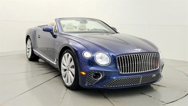 A blue Bentley Continental GTC convertible graces the showroom floor with its top down, showcasing a chrome grille and large alloy wheels—a true luxury tourer in every sense.