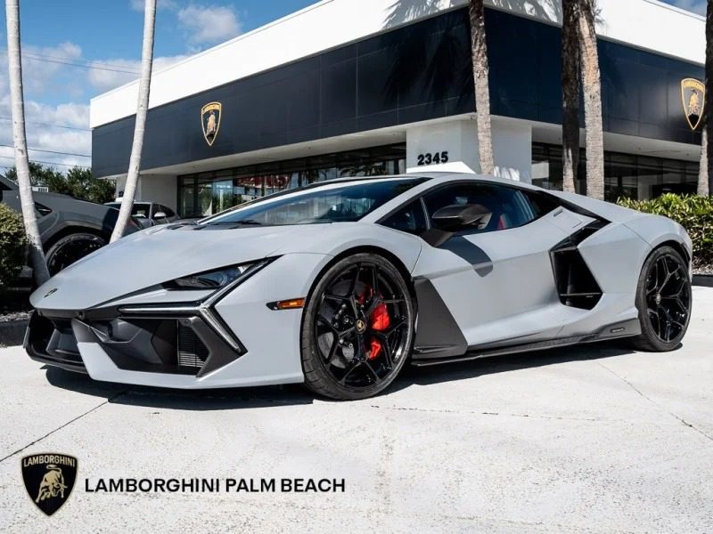 A sleek 2024 Lamborghini Revuelto sports car is parked in front of a dealership, framed perfectly by palm trees swaying gently in the background.